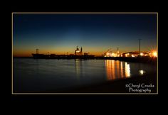 the sun is setting behind a large ship in the water and lights are reflected on the water