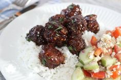 a white plate topped with meatballs and rice next to cucumber, carrots and other veggies