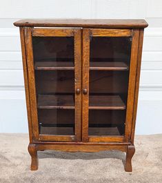 an old wooden cabinet with glass doors on the top and bottom shelves, in front of a white wall