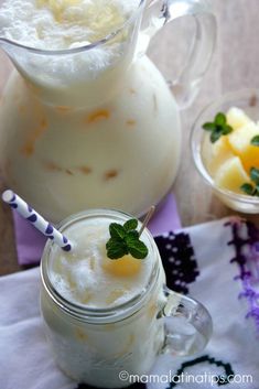 two glasses filled with drinks sitting on top of a table next to another glass pitcher