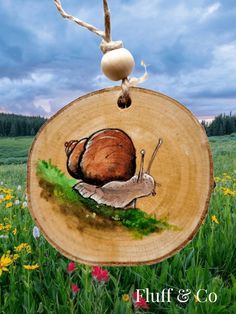 a painting of a snail on a piece of wood with grass and flowers in the background