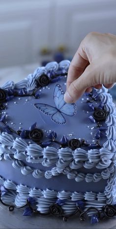 a hand is touching the frosting on a blue heart shaped cake with black roses