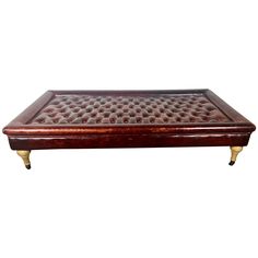 a brown leather ottoman with brass legs and foot rests on an isolated white background for use as a coffee table