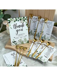 wedding stationery with gold spoons and place cards on a wooden tray next to greenery