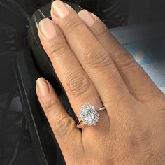 a woman's hand with a diamond ring on her left hand, and a car in the background