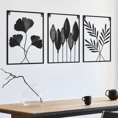 three metal wall art pieces hanging on a white wall above a wooden table with a vase and coffee cup