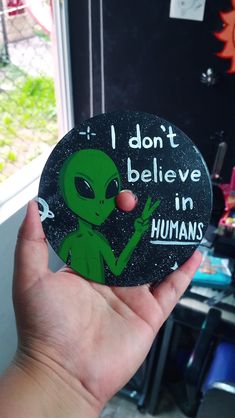 a hand holding up a button with an alien saying i don't believe in humans