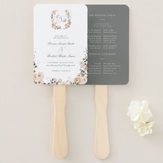 a wedding fan with flowers on it next to a flowery bouquet and two wooden utensils