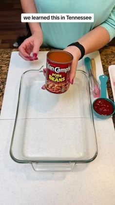 a woman holding a can of canned beans on top of a counter with other ingredients