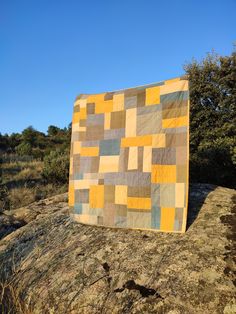 a patchwork quilt sitting on top of a rock in the middle of a field