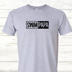 Show off your pride in your swimming child with this crew neck tee from Swim Mom Customs, a mother-daughter small business. Featuring a stylish & playful black font design, it's made from high-quality materials in a variety of sizes from XS to 5XL. Show your support and make memories in this perfect tee for any swim papa! Customize the shirt by adding text to the back for $3 Fitted Gray T-shirt With Letter Print, Fitted Short Sleeve T-shirt For Father's Day, Unisex Black T-shirt For Father's Day, Black Unisex T-shirt For Father's Day, Gray Letter Print T-shirt, Casual Fitted Tops For Father's Day, Fitted Casual Tops For Father's Day, Unisex Pre-shrunk T-shirt For Father's Day, Unisex Name Print T-shirt For Summer