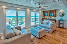 a living room filled with furniture next to an ocean side kitchen and covered in windows