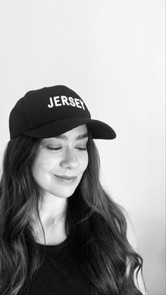 a black and white photo of a woman with long hair wearing a baseball cap that says jersey