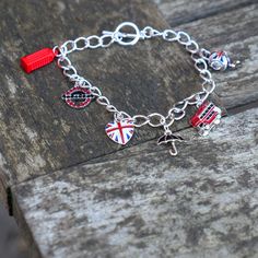 Union Jack and iconic British symbol charm bracelet, with hand finished enameled charms. The bracelet is made up of six charms: A Union Jack enamel heart, a rhinestone tube symbol, an enamel red London bus, a black enameled umbrella, a red enameled telephone box and an enameled Union Jack teapot.  Designed by us, at our London office. This beautiful kitsch charm bracelet celebrates the best of British. Wear a Union Jack with pride for any occasion you fancy. Bracelet: (L) 192mm Each item is presented on a recycled paper gift card (as shown), packed in biodegradable bags and then placed in an eco-friendly envelope (also shown). Orders are sent in 100% recyclable paper padded envelopes, to keep the jewellery safe during delivery.   The bracelet does up with a T-Bar fastening. This is just on Metal Charm Bracelet With Logo For Gift, Metal Charm Bracelet With Logo As Gift, Red Enamel Bracelet Jewelry, Enamel Charms Bracelet, Metal Bracelet With Logo Charm As A Gift, Metal Bracelets With Logo Charm As Gift, Enamel Bracelet With Lobster Clasp, Enamel Bracelet Jewelry With Lobster Clasp, Red Metal Charm Bracelet