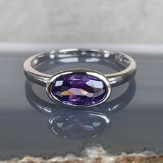 Introducing a stunning amethyst ring, set in sterling silver with a slender oval lab-grown gemstone. These rings are brand new, sourced from a jeweler's vintage estate collection, adding a touch of history and uniqueness to each piece. Available in three sizes: 6, 7, and 8, ensuring a perfect fit for your finger. When placing your order, please specify your preferred size to ensure you receive the perfect ring for you. Amethyst, with its deep purple hue, is not only a symbol of luxury and elegan Modern Crystal Ring With Oval Gemstone, Elegant Amethyst Bezel Set Oval Cabochon Ring, Elegant Amethyst Oval Cabochon Ring With Bezel Setting, Modern Oval Crystal Ring With Gemstone, Elegant Sterling Silver Amethyst Ring Oval Cabochon, Classic Amethyst Birthstone Ring, Fine Jewelry Oval Birthstone Ring In Sterling Silver, Oval Sterling Silver Birthstone Ring With Center Stone, Oval Sapphire Ring In Sterling Silver