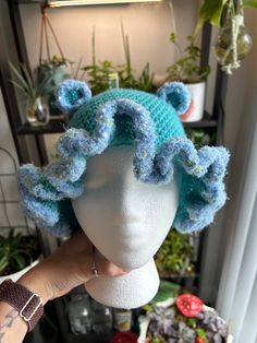 a person holding up a knitted hat on top of a mannequin head