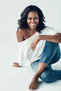 a woman in white shirt and jeans sitting on the ground with her legs spread out