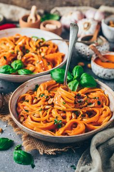 two bowls filled with pasta and basil on top of a table