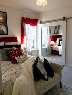 a bedroom with a white bed and red curtains on the window sill next to a mirror