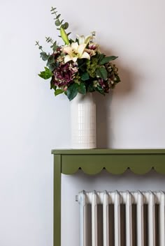 a vase filled with flowers sitting on top of a green table next to a radiator