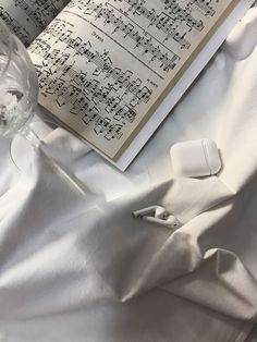 an open book with musical notations on it next to a wine glass and headphones