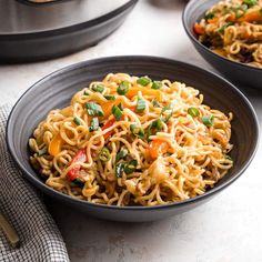 two black bowls filled with noodles and veggies next to a plate of bread