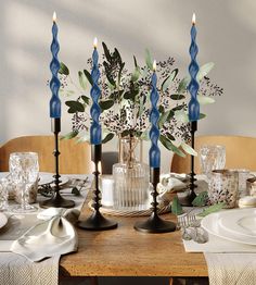 a dining room table set with blue candles and flowers in a vase on the centerpiece