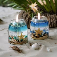 two candles are sitting on the sand with shells and starfish in them next to each other