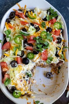 a white plate topped with a taco casserole covered in cheese and black olives