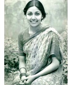 an old photo of a woman sitting in the grass with her hands crossed and smiling