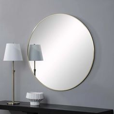 a round mirror sitting on top of a black table next to a lamp and lampshade