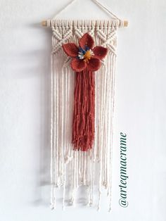 a red and white wall hanging with flowers on the front, one flower has been made from yarn