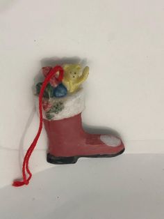 an ornament is hanging from a red string on a white wall with a bear in a boot