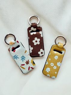 three keychains with flower designs on them sitting on a white cloth covered surface