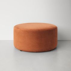 an orange round ottoman sitting on top of a white floor next to a gray wall