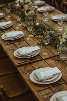 the table is set with white plates and place settings, silverware and greenery