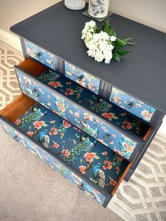 a blue dresser with flowers on it and an open drawer in the bottom half is shown