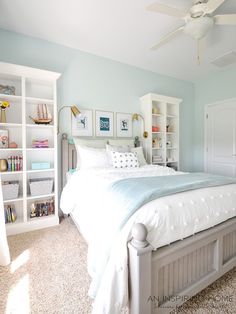 a white bed sitting in a bedroom next to a book shelf filled with lots of books