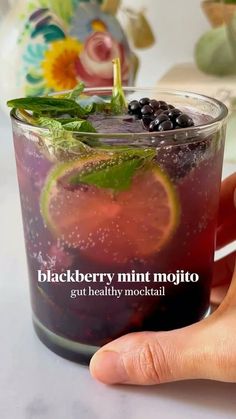 a hand holding up a glass filled with black berry mint mojito