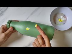 a person holding a green bottle with yellow dots on it next to a bowl and spoon