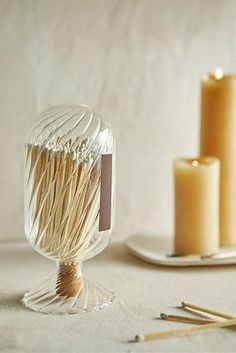 a glass vase filled with matches on top of a table next to two candles and some sticks