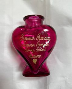 a pink heart shaped glass vase with writing on the bottom and inside, against a white background