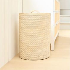 a basket sitting on the floor in front of a white dresser with drawers behind it