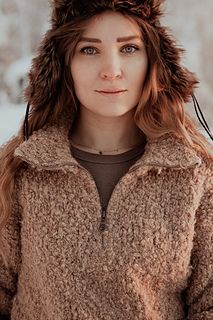 a woman with long hair wearing a furry coat in the snow, looking at the camera