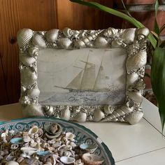 an old photo frame with seashells in front of it on a table next to a potted plant