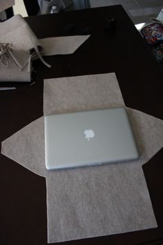 an apple laptop sitting on top of a table next to some brown paper and scissors