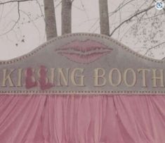 a sign that says kissing booth with trees in the backgroung and pink drapes