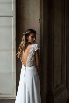 a woman standing in front of a wall wearing a white dress with an open back