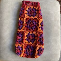 an orange and purple crocheted object laying on top of a white chair next to a wall