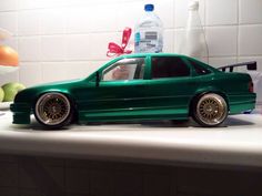 a green toy car sitting on top of a counter next to a bowl of fruit